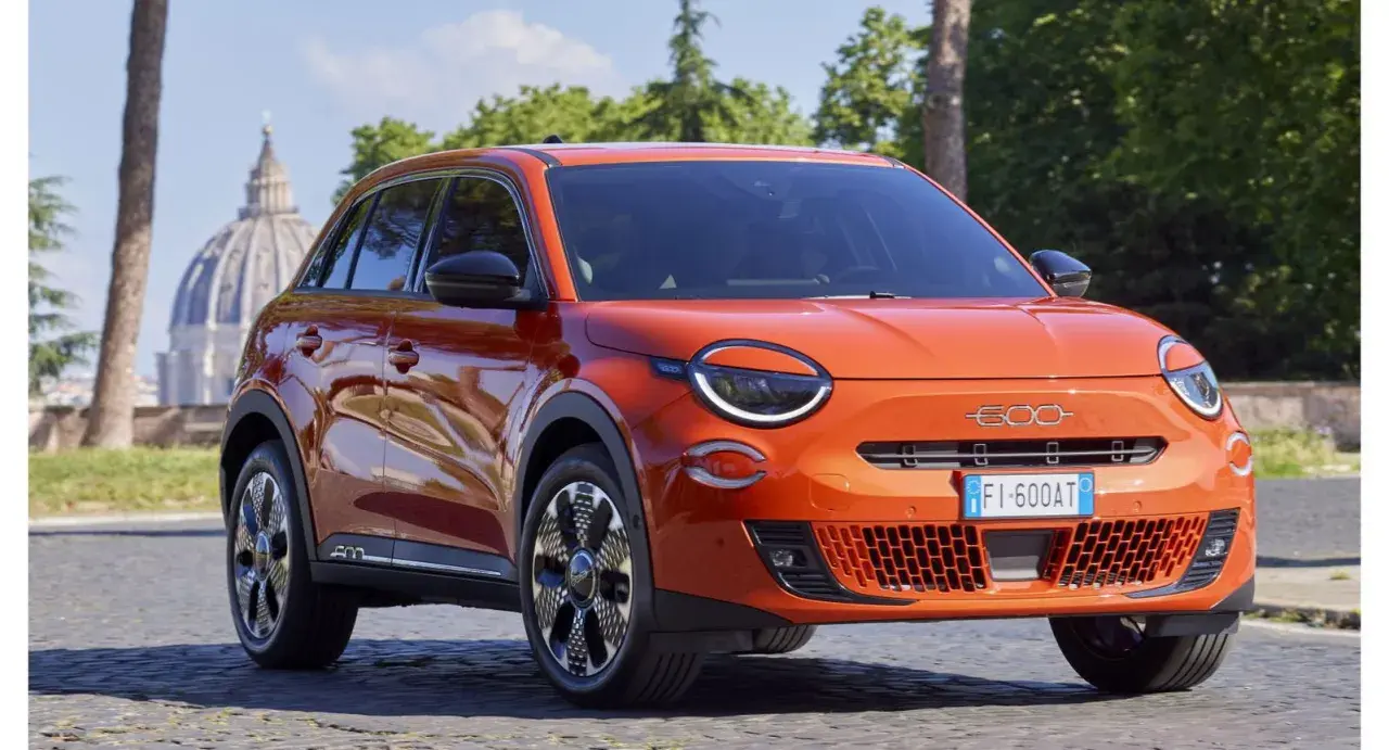 El nuevo Fiat 600, un SUV naranja vibrante, se exhibe con elegancia frente a la cúpula de San Pedro en Roma.