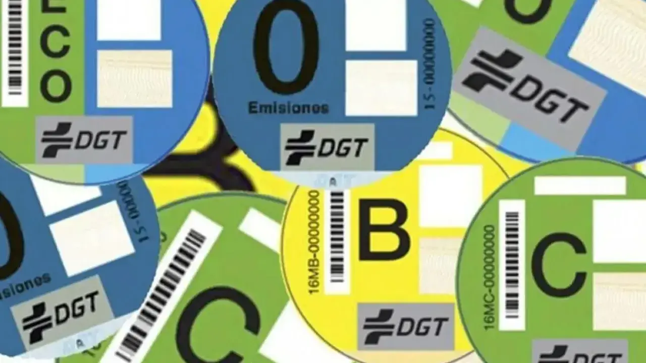 Varias etiquetas DGT circulares de diferentes colores (azul, verde, amarillo) con letras (ECO, 0, B, C) y códigos de barras, indicando la clasificación ambiental de vehículos.