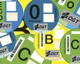 Varias etiquetas DGT circulares de diferentes colores (azul, verde, amarillo) con letras (ECO, 0, B, C) y códigos de barras, indicando la clasificación ambiental de vehículos.