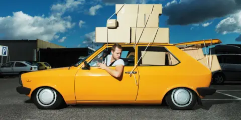 Hombre en coche amarillo cargado de cajas, preguntándose cuanto peso aguanta un coche.