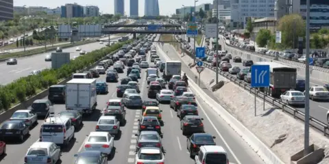 Congestión vehicular en una autopista, reflejo de la movilidad urbana. Coches y camiones detenidos en múltiples carriles bajo un cielo despejado.