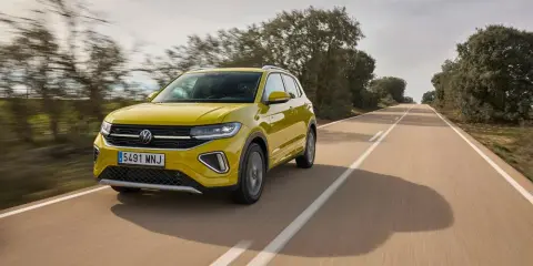 Un coche amarillo Volkswagen T-Cross circula por una carretera rural. ¿Cuánto se tarda en fabricar un coche? ¡Este parece listo para la carretera!