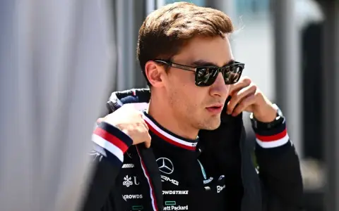 George Russell ajustándose la chaqueta, con gafas de sol y el logo de Mercedes.