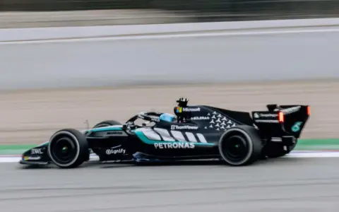 El Aston Martin AMR26 negro y turquesa acelera en la pista, con el logo de Petronas visible.