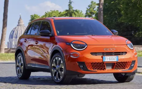El nuevo Fiat 600, un SUV naranja vibrante, se exhibe con elegancia frente a la cúpula de San Pedro en Roma.