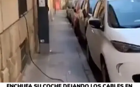 Un coche eléctrico se carga en la calle, con cables cruzando la acera. Una forma poco convencional de como cargar coche electrico en la calle.