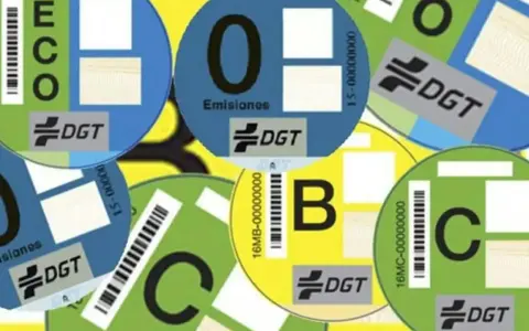 Varias etiquetas DGT circulares de diferentes colores (azul, verde, amarillo) con letras (ECO, 0, B, C) y códigos de barras, indicando la clasificación ambiental de vehículos.