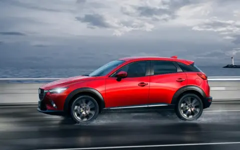 Un Mazda CX-3 rojo circula por una carretera mojada junto al mar. Las medidas del Mazda CX-3 son ideales para la ciudad y la aventura.