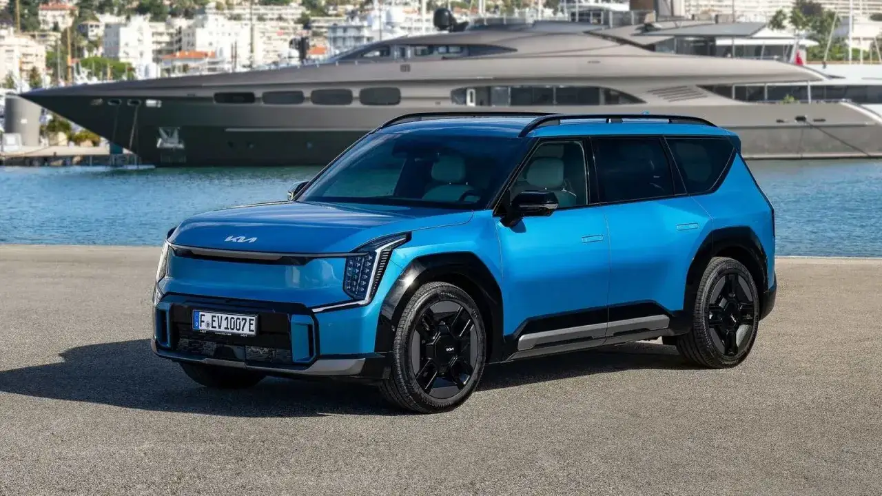 Un SUV azul el&eacute;ctrico, uno de los coches c&oacute;modos ideales para explorar la costa, aparcado frente a un yate de lujo y un puerto.