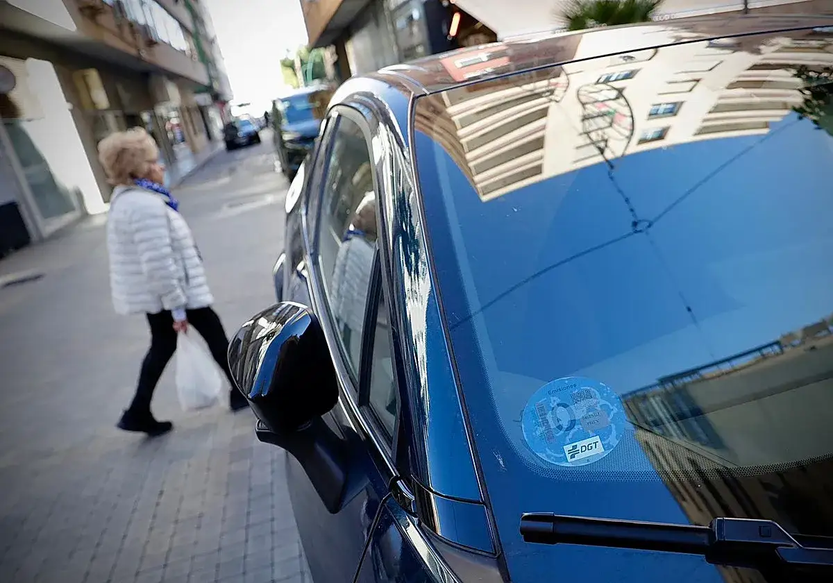 Una mujer cruza la calle mientras un coche el&eacute;ctrico, con pegatina DGT, espera. Los coches el&eacute;ctricos pagan zona azul.