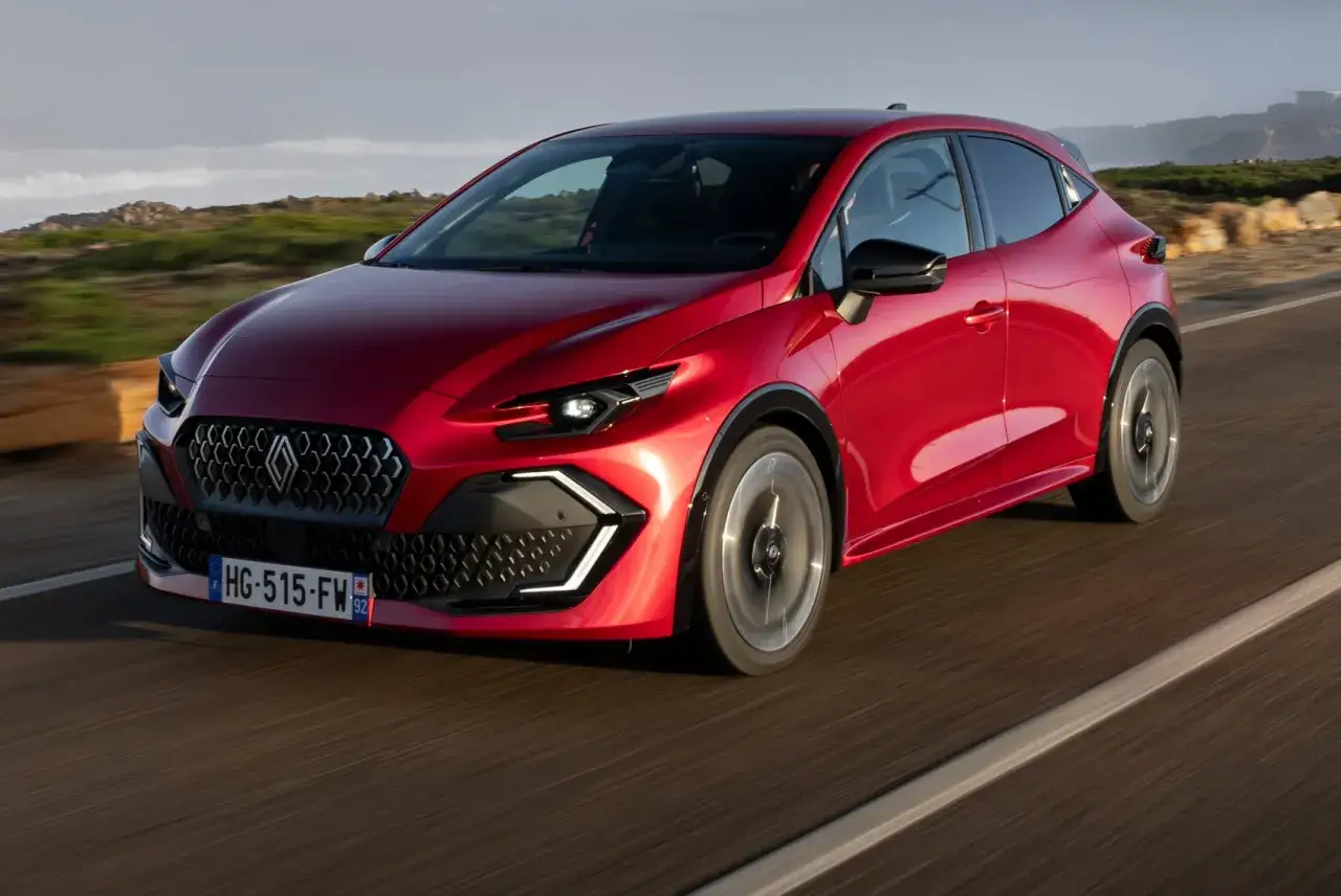 El nuevo Clio 2026, un coche rojo brillante, avanza por una carretera costera con un diseño moderno y deportivo.