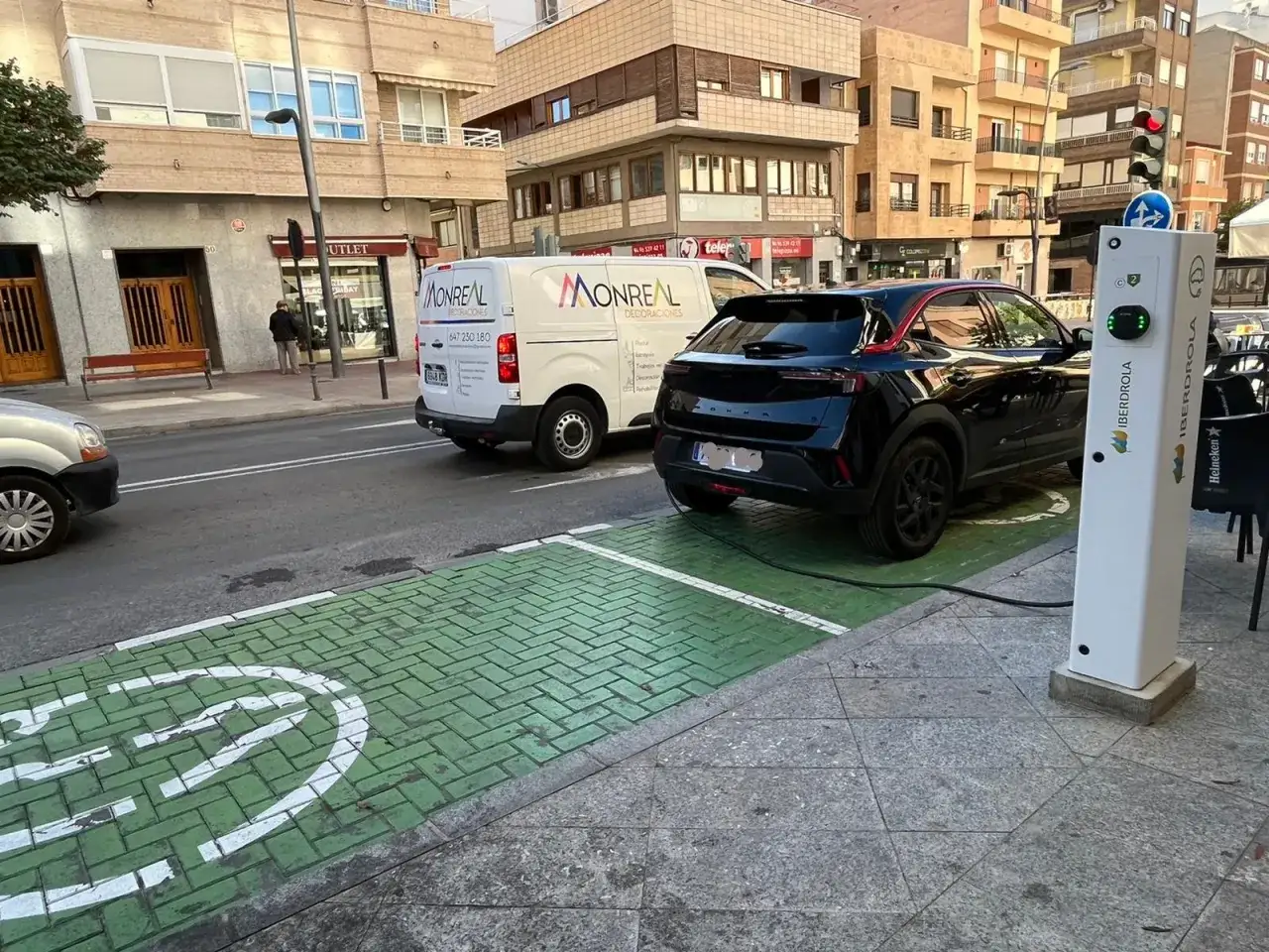 Coche eléctrico negro cargando en la calle, en una zona verde con señal de carga. Así se ve como cargar coche electrico en la calle.