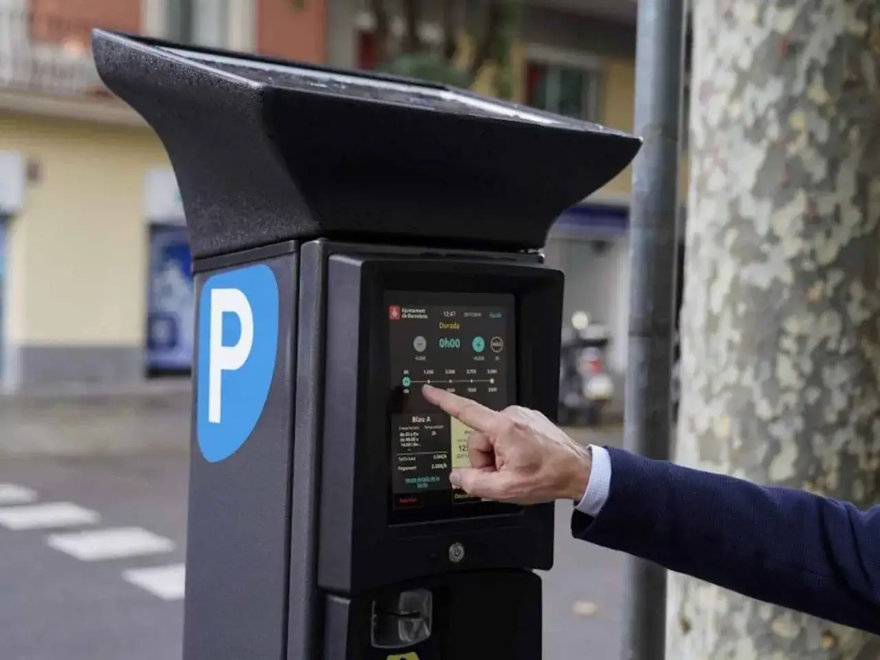 Un hombre usa un parquímetro para el pago de la zona azul en Barcelona. La pantalla muestra opciones de duración y tarifas.