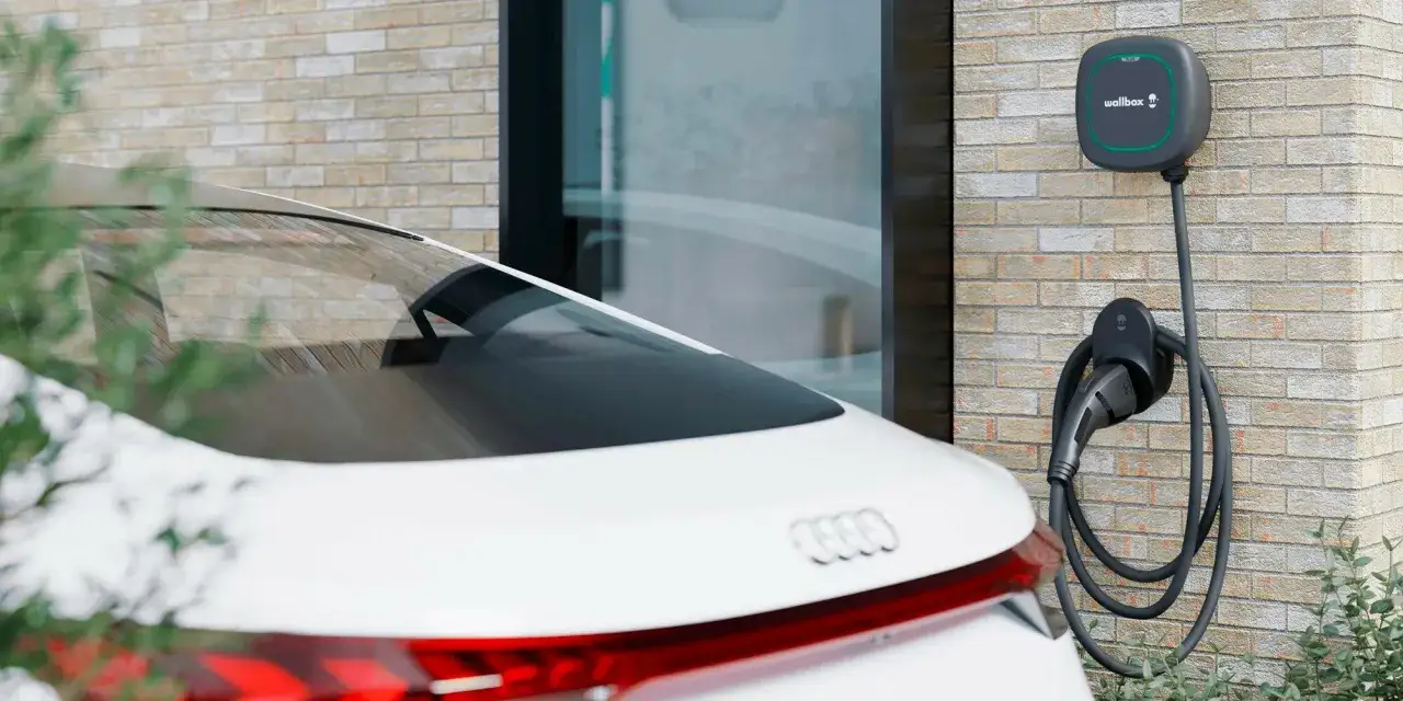 Cargador de coche eléctrico en pared de ladrillo, listo para responder cuanto tarda en cargar un coche eléctrico en casa.