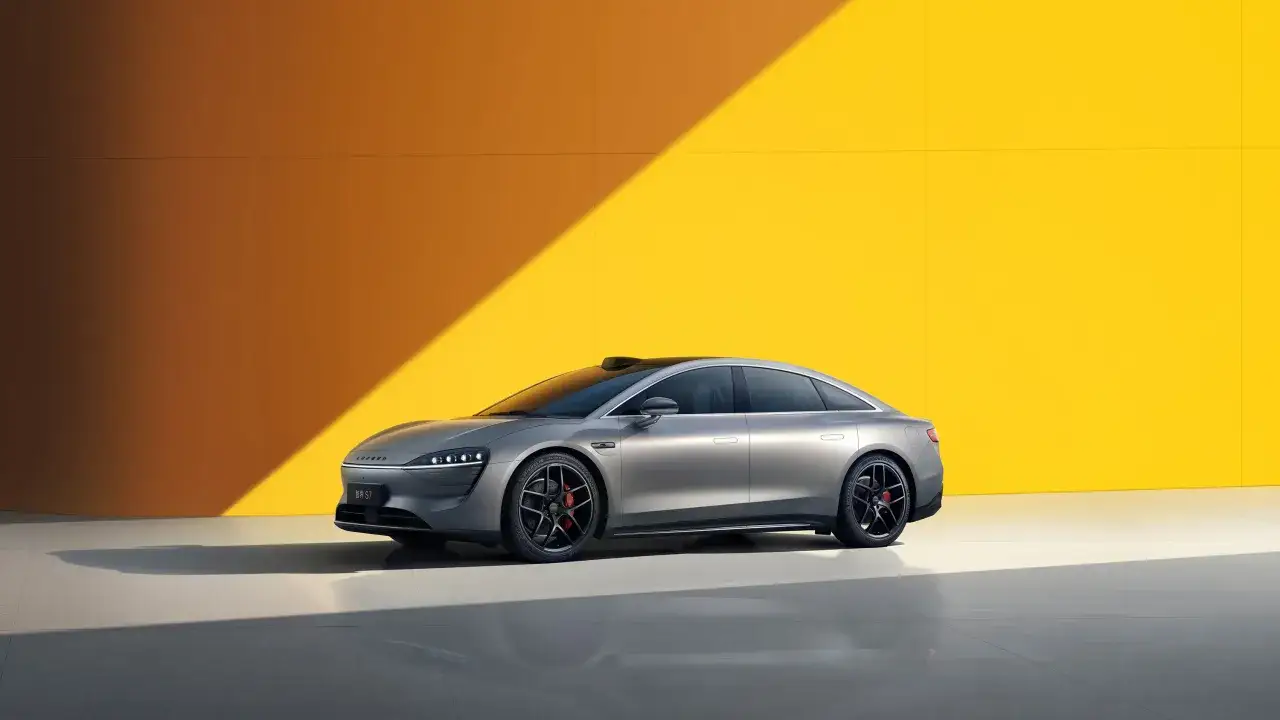 Coche el&eacute;ctrico gris, un modelo de coche Huawei con dise&ntilde;o futurista, aparcado frente a una pared amarilla con luz solar.