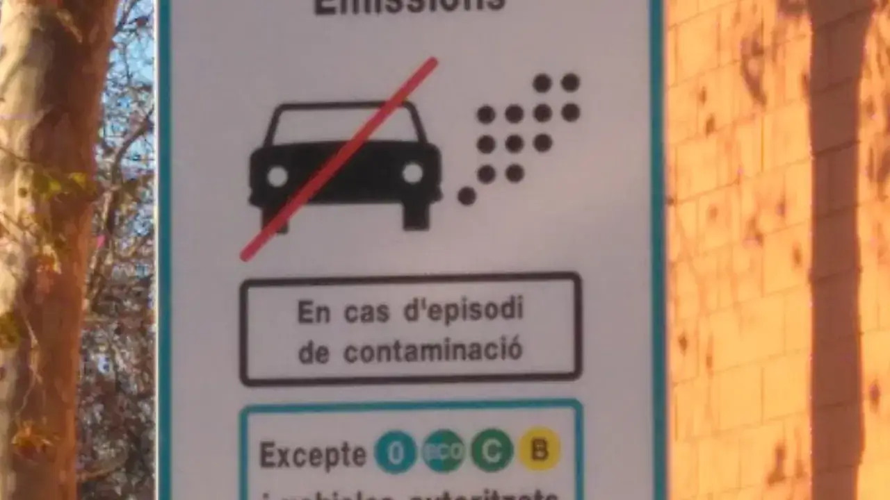 Señal de tráfico que indica qué quins cotxes poden entrar a Barcelona. Muestra un coche con una línea roja cruzada sobre las emisiones, indicando restricciones.