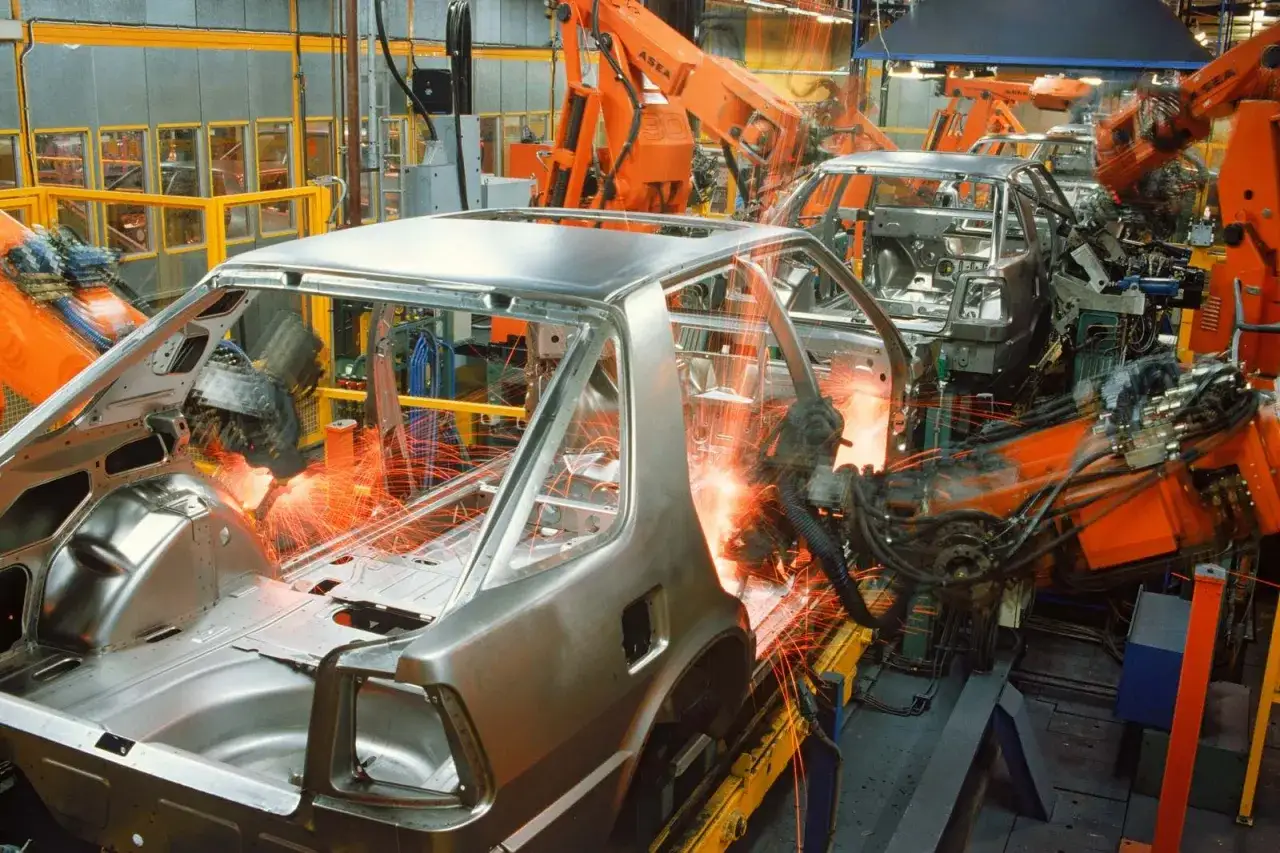 Robots sueldan carrocerías de coches en una fábrica. Así se responde a cuanto se tarda en fabricar un coche.