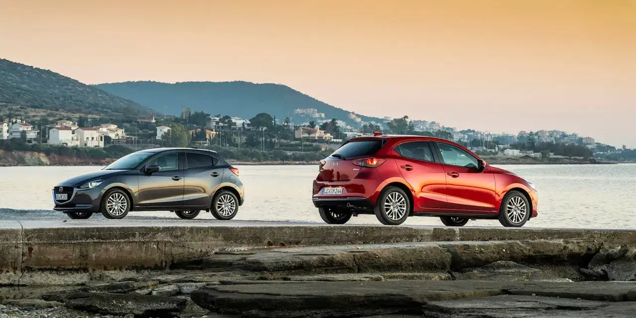 Dos Mazda, uno gris y otro rojo, lucen su dise&ntilde;o en un muelle. La fiabilidad Mazda se siente en cada curva.