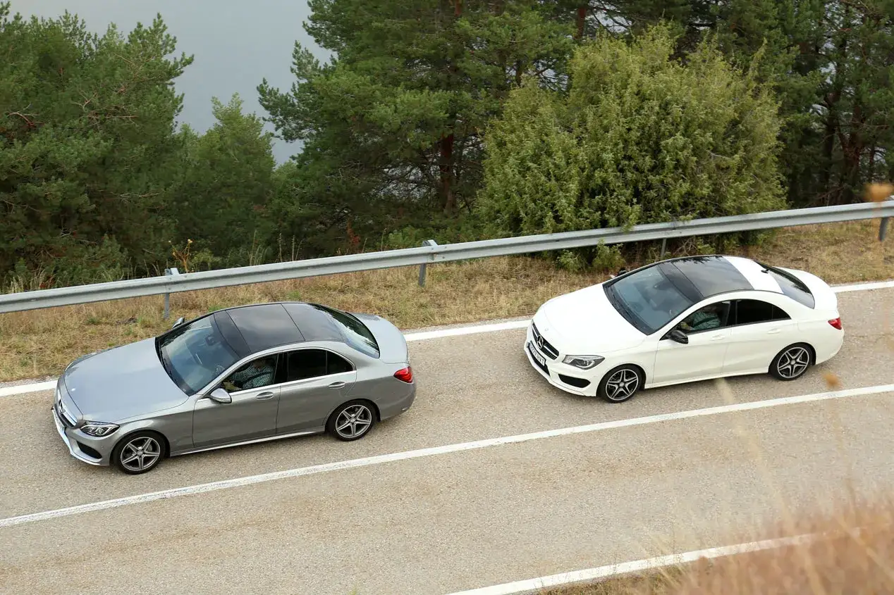 Dos Mercedes, un Clase C gris y un Clase E blanco, circulan por una carretera rodeada de árboles.